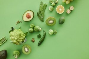 Top-down view of assorted fresh green vegetables and fruits on a vibrant green background.