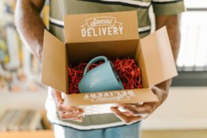 Man holding a box with a special delivery coffee mug inside.